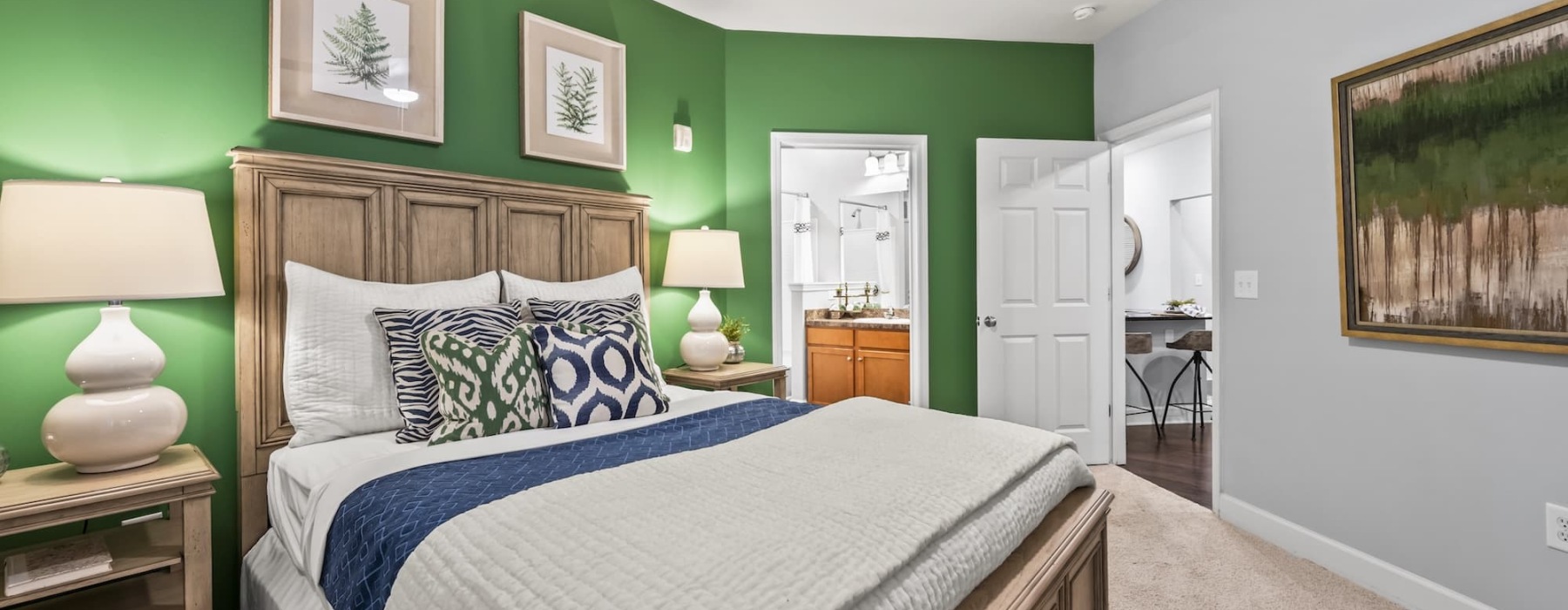 South Asheville, NC, Pet-Friendly Apartments - Weirbridge Village - Bedroom With Green Accent Wall, Wooden Bed Frame, Patterned Pillows, Two Bedside Lamps, and Carpeted Floor.
